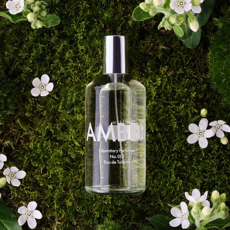 Lifestyle shot top view of Laboratory Perfumes Amber Eau de Toilette (100 ml) on grass with white flowers in the background