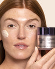 Model holding Yon-Ka Paris Excellence Code Creme (50 ml) with product smear on cheek to show color and texture