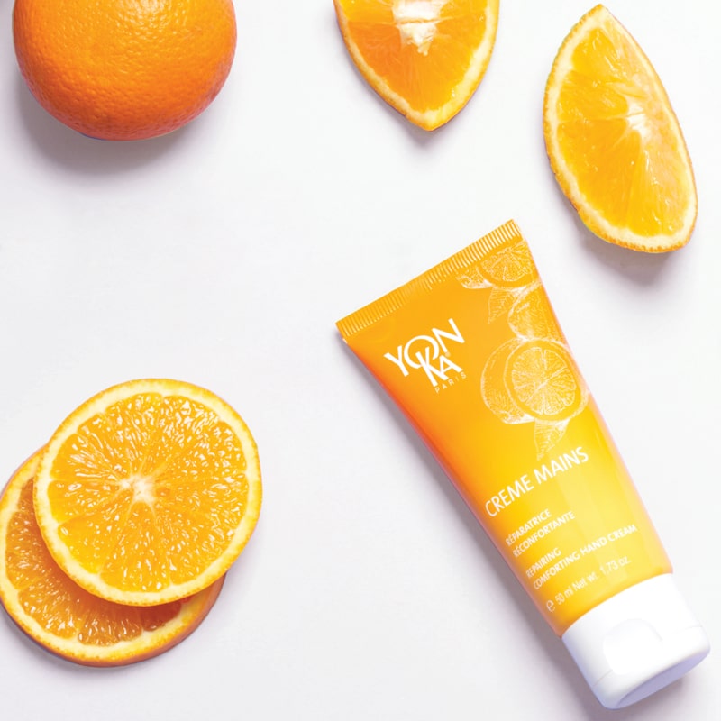 Top view of Yon-Ka Paris Creme Mains - Vitalite Sweet Orange (50 ml) with oranges in the background