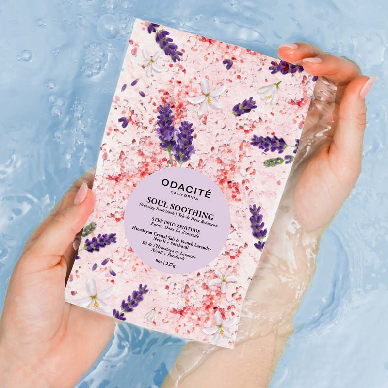 Close up of model holding Odacite Soul Soothing Relaxing Bath Soak (8 oz) with bath water in the background