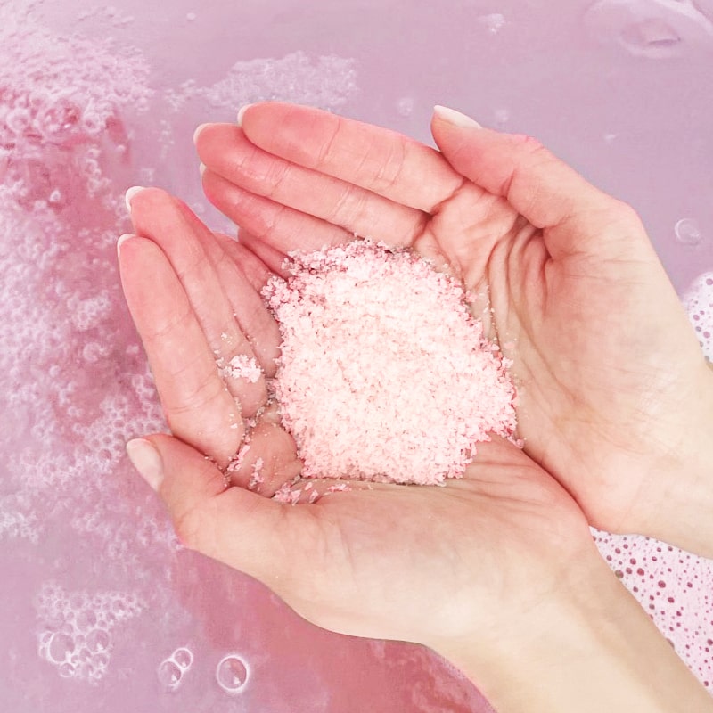 Close up of model holding in hands Odacite Soul Soothing Relaxing Bath Soak (8 oz) with bath water in the background