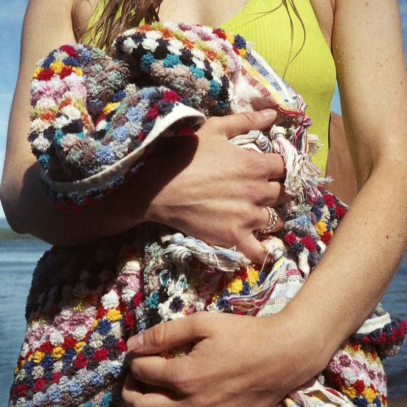 Close up of model holding Bathing Culture Cosmic Rainbow Towel (Deadstock) with beach in the background