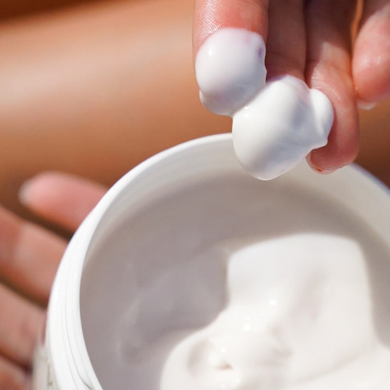 Close up shot of Carthusia A’mmare Body Lotion (250 ml) with lid off and model showing color and texture of lotion on fingertips