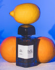 Lifestyle shot of BDK Parfums Villa Neroli Eau de Parfum (100 ml) with lemon on top of bottle and oranges in the background