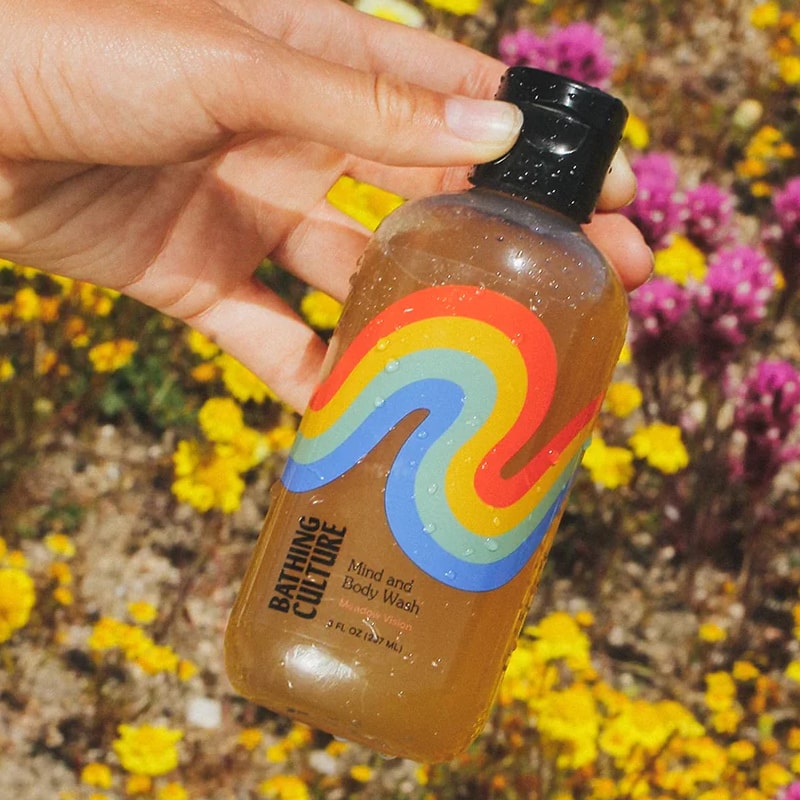 Close up shot of model holding Bathing Culture Meadow Vision Mind and Body Wash (8 oz) with meadow flowers in the background