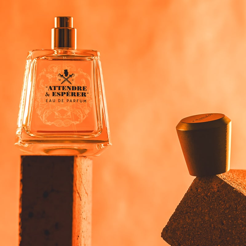 Lifestyle shot of Frapin Attendre &amp; Esperer Eau de Parfum with cap off sitting on the end of a brick and bright orange background