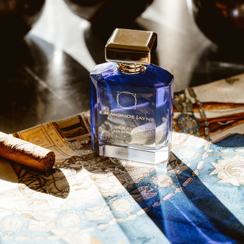 Ormonde Jayne Verano Eau de Parfum - perfume bottle and cigar sitting on cloth on stone table