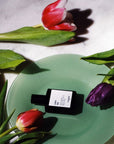 Versatile Paris Culot The (Tea Cap) Extrait de Parfum on a plate surrounded by tulips
