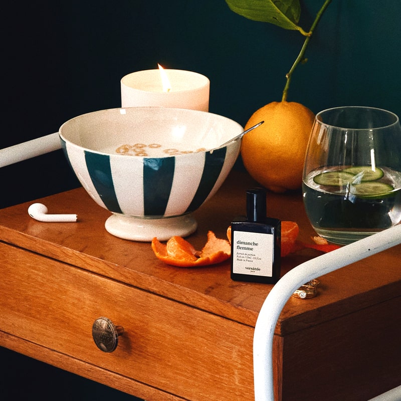 Versatile Paris Dimanche Flemme (Lazy Sunday) Extrait de Parfum on a side table with bowl of cereal, tangerine and cucumber water