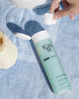 Lifestyle shot of Yon-Ka Paris Gel Nettoyant (200 ml) with model holding cotton ball near the top of the bottle with lid open 
