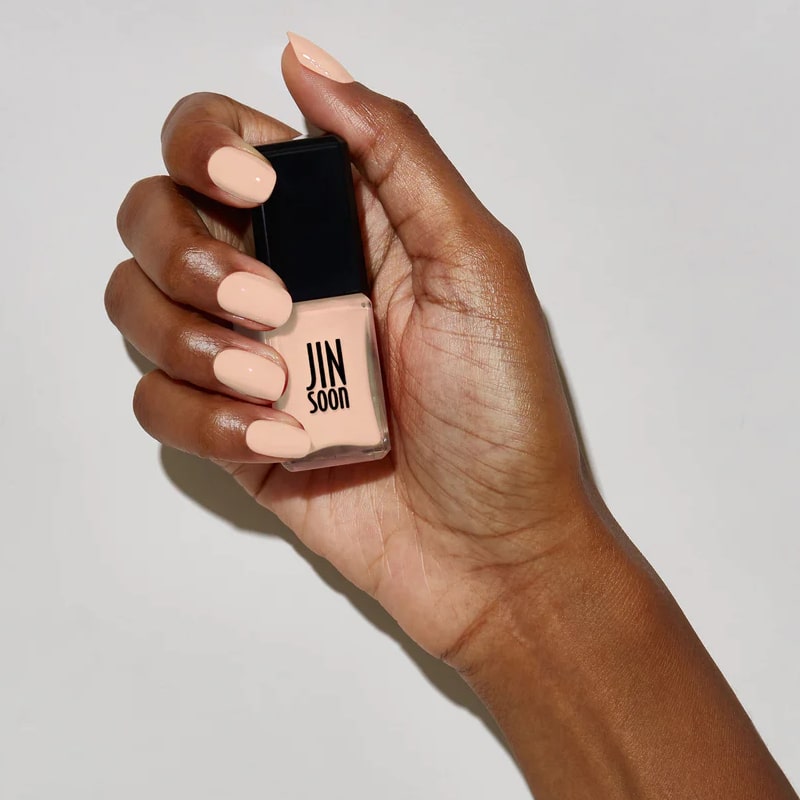 Model with dark skin tone wearing and holding bottle of JINsoon Nail Lacquer - Nostalgia