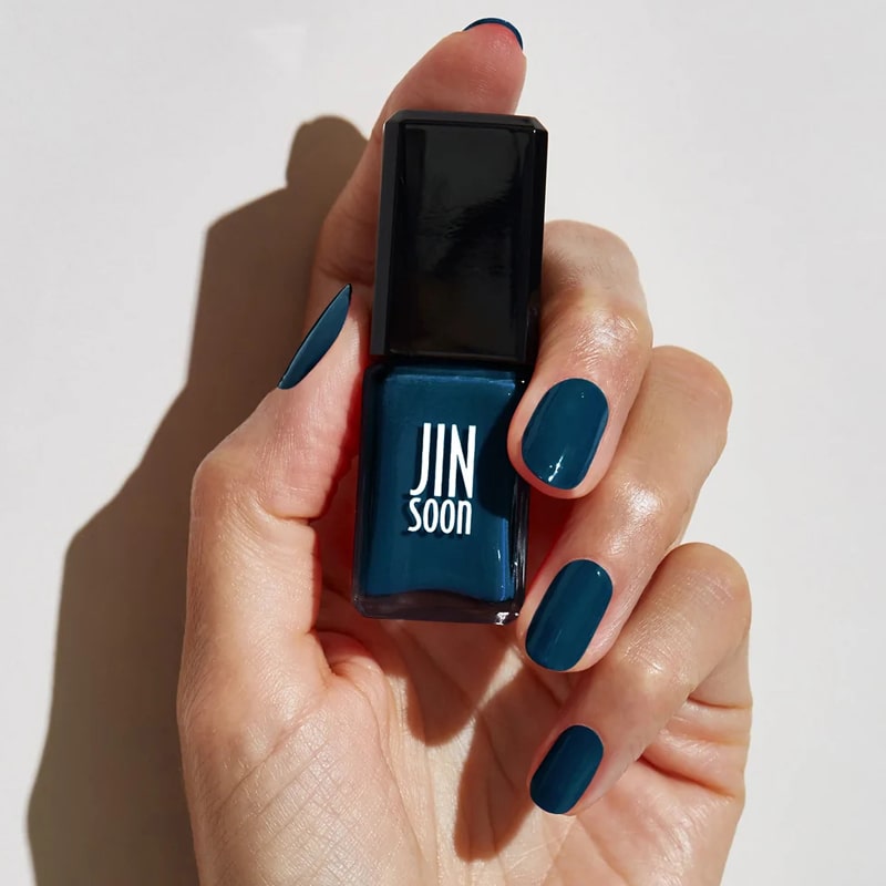 Model with light skin tone wearing and holding bottle of JINsoon Nail Lacquer - Beau
