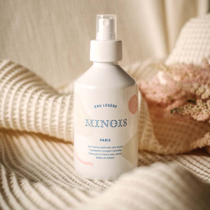 Lifestyle shot of Minois Paris Eau Legere (Light Water) (250 ml) with blanket and flowers in the background