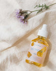 Lifestyle shot of Minois Paris Huile Seche (Dry Oil) (150 ml) with purple flowers in the background