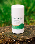 Lifestyle shot of Ursa Major Forest Fix Deodorant (2.6 oz) on tree stump and grass in the background