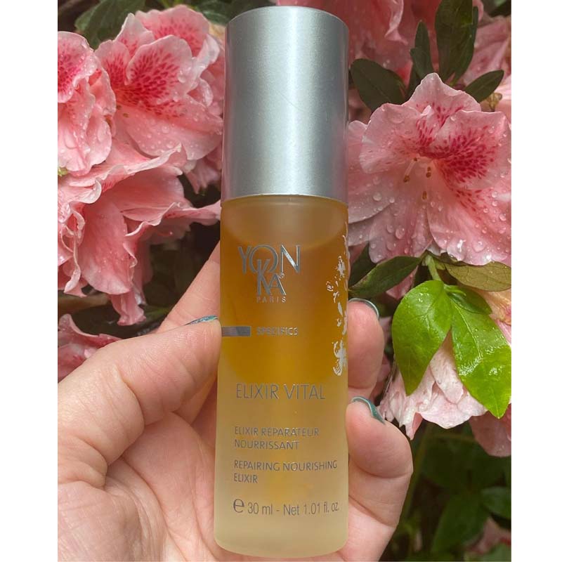 Yon-Ka Paris Elixir Vital (30 ml) in hand of model with pink flowers in the background