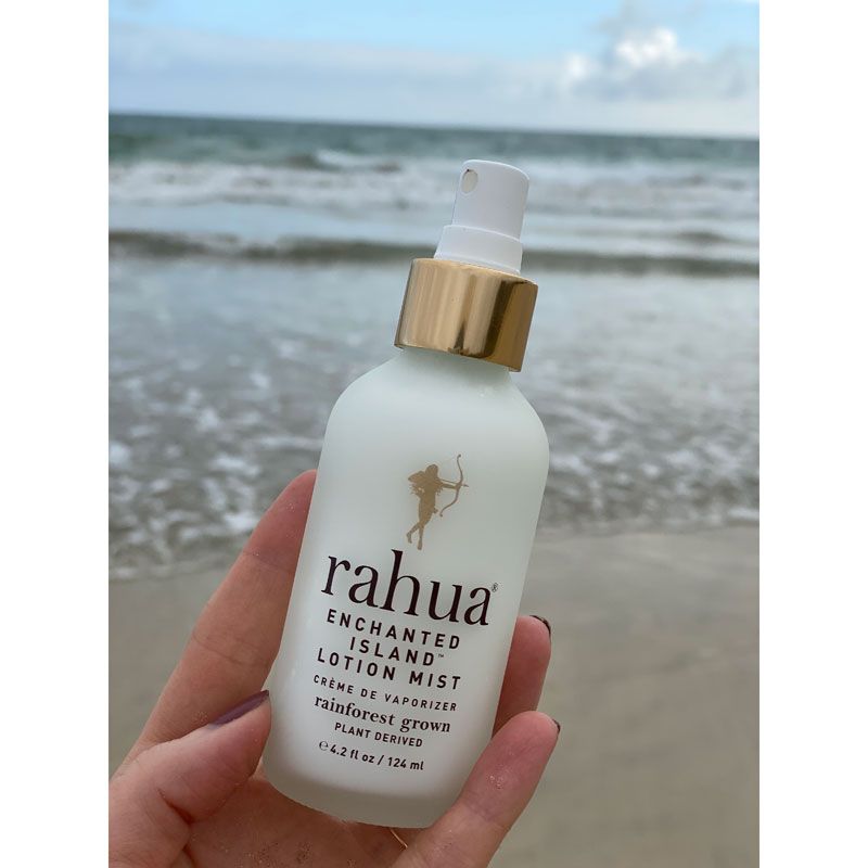 Rahua by Amazon Beauty Rahua Enchanted Island Lotion Mist held in front of the beach in background