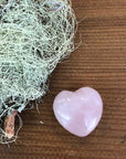 Nomads and Settlers Rose Quartz Heart Stone lifestyle shot with rose heart beside green plant material