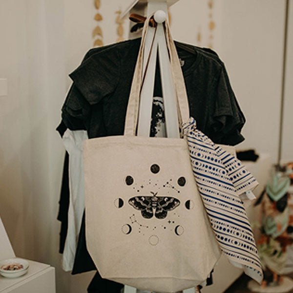 Mineral and Matter Moth and Moons Tote Bag - shown hanging on a rack with clothing and with a scarf tied for flair (not included)