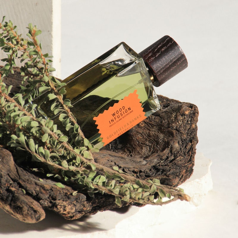 Goldfield & Banks Wood Infusion Perfume showing with a piece of wood and plant