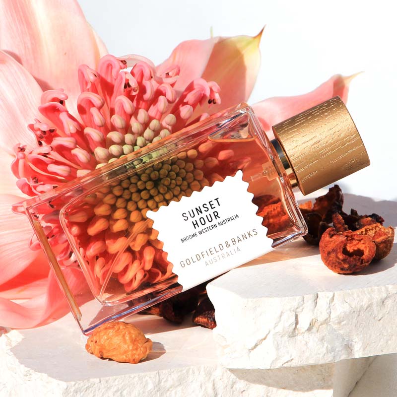 Beauty shot of Goldfield &amp; Banks Sunset Hour Perfume 100 ml on stone slabs with large pink flower in the background