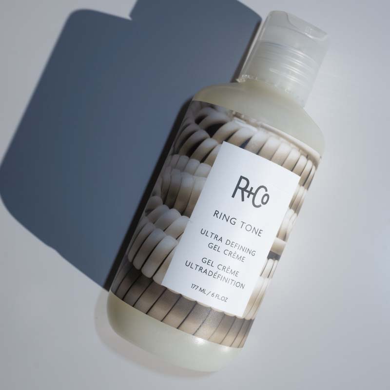 R+Co Ring Tone Curl Cream showing bottle laying on back with shadow