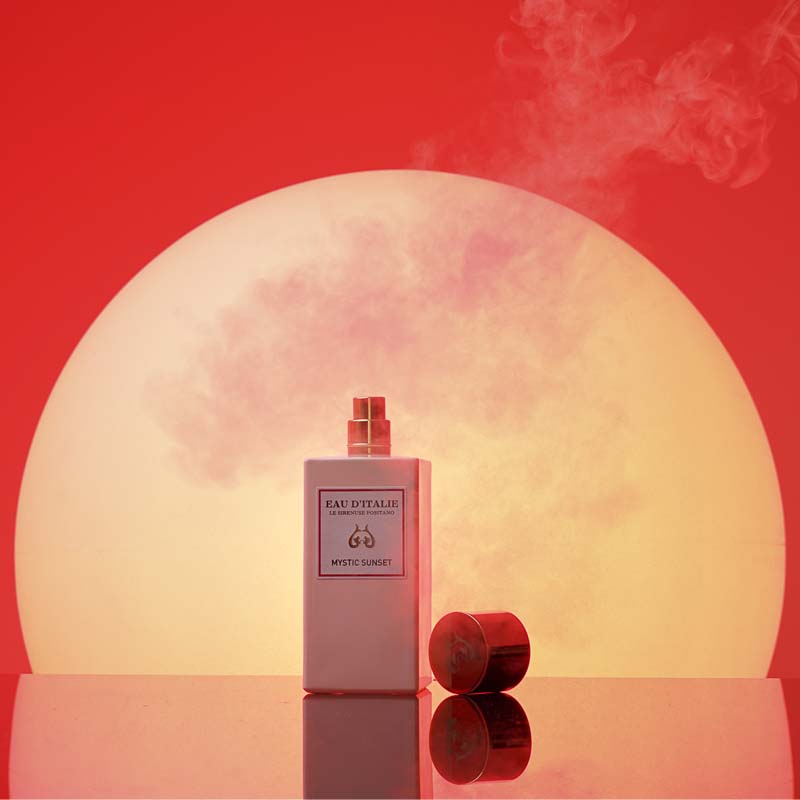 Eau d'Italie Mystic Sunset Eua de Parfum Spray showing with lid sitting next to bottle in front of a mystic sunset