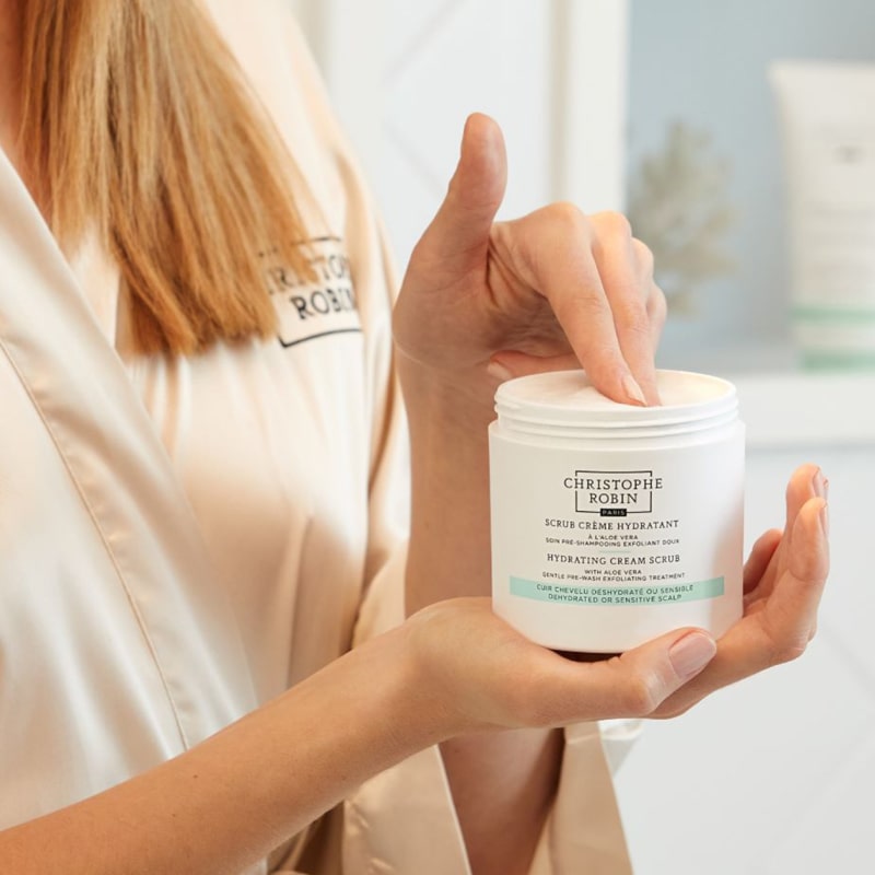 Christophe Robin Hydrating Cream Scrub showing in models hand with model taking scoop of scrub with fingers