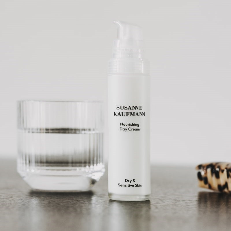 Susanne Kaufmann Nourishing Day Cream - lifestyle shot of product between a glass of water  and a hair clip