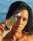 Rahua by Amazon Beauty Scalp & Skin Toner in Model's hand - ocean in background