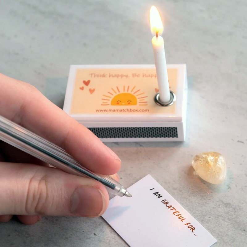 Marvling Bros Ltd Hello Sunshine Mindfulness Gift In A Matchbox showing lit candle in box and hand writing a note by the Citrine stone.
