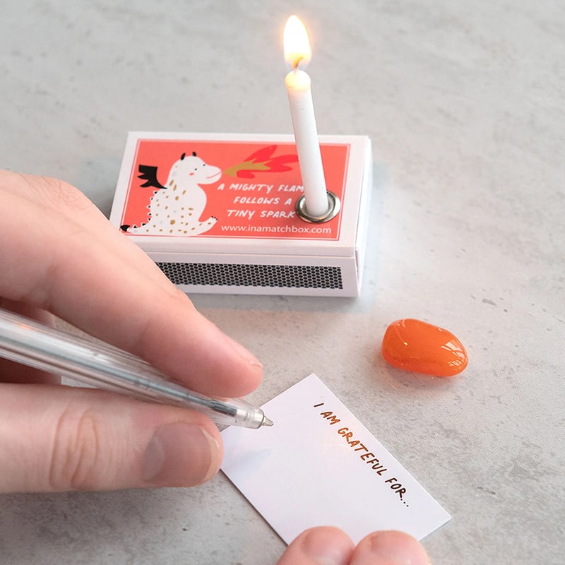 Marvling Bros Ltd Your Fire Can Light The World Mindfulness Gift showing model&#39;s hands writing a note with candle burning