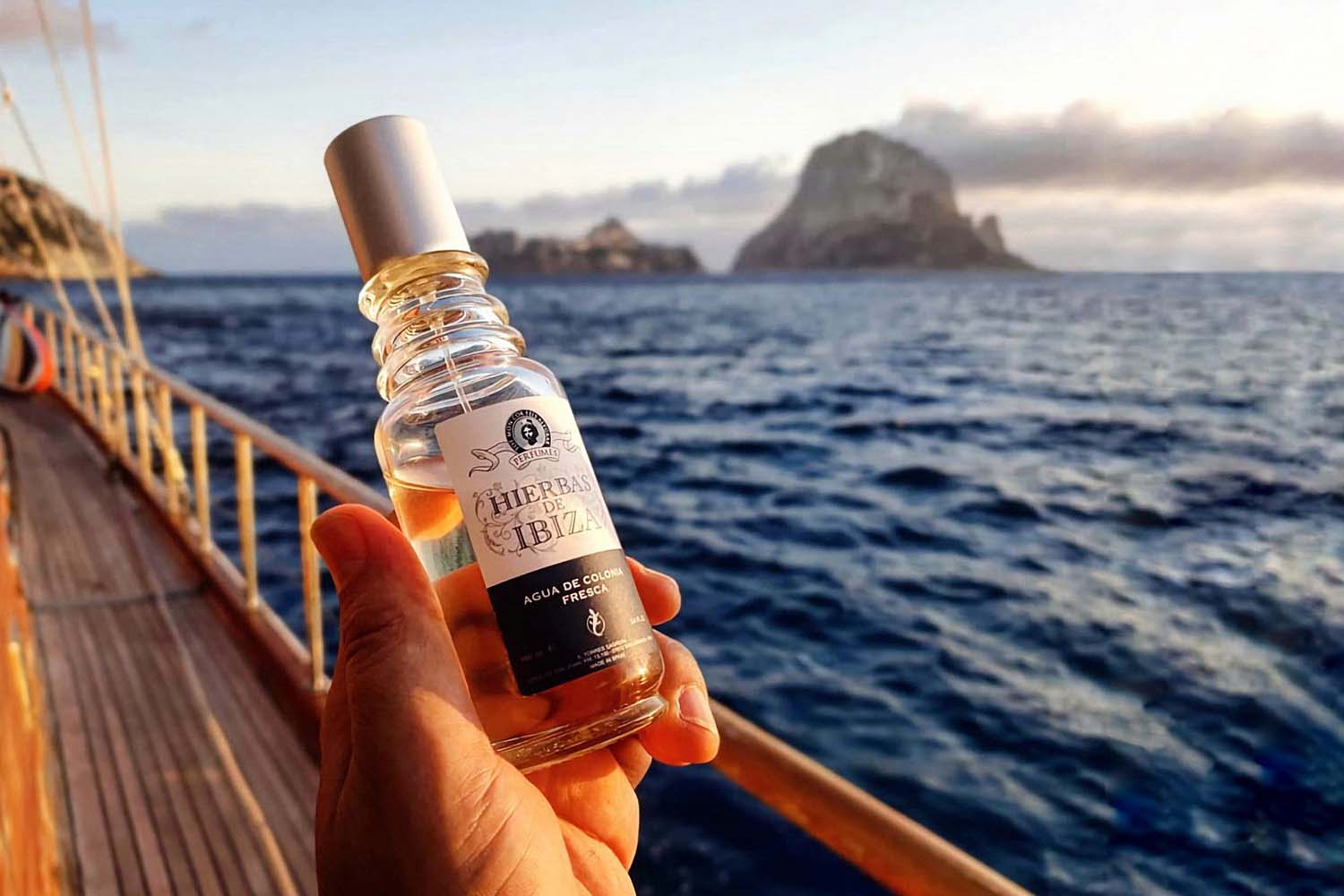 Hierbas de Ibiza Agua de Colonia Fresca bottle in hand of model on a yacht on the ocean with islands in the background