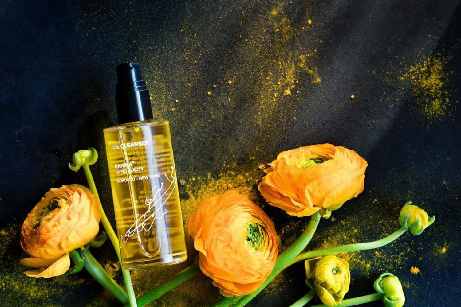 beauty shot top view of Oil Cleanser by Kahina Giving Beauty on black slate background with tumeric and orange flowers