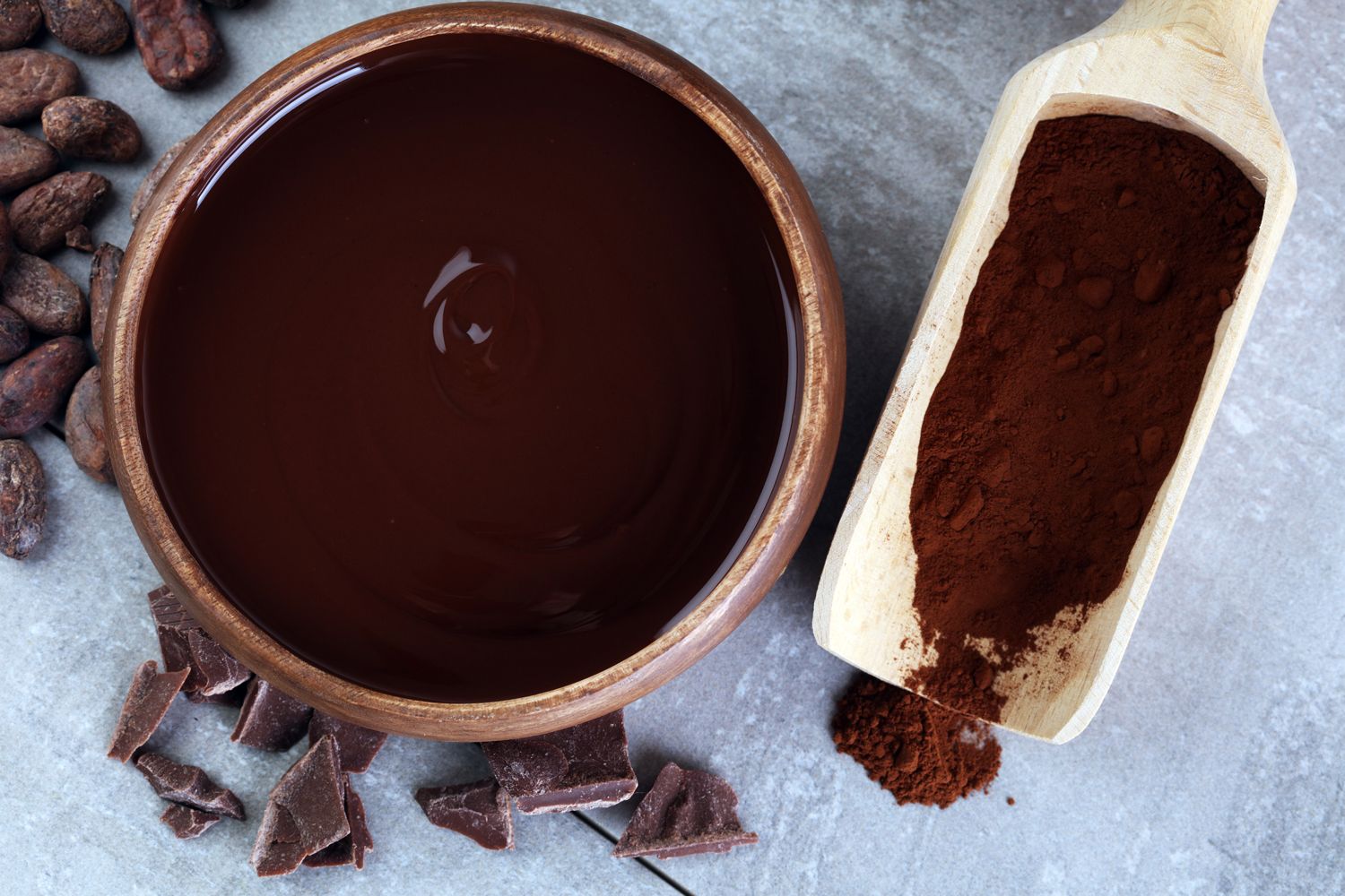 Chocolate pieces, melted chocolate and scoop with cocoa powder shown top view