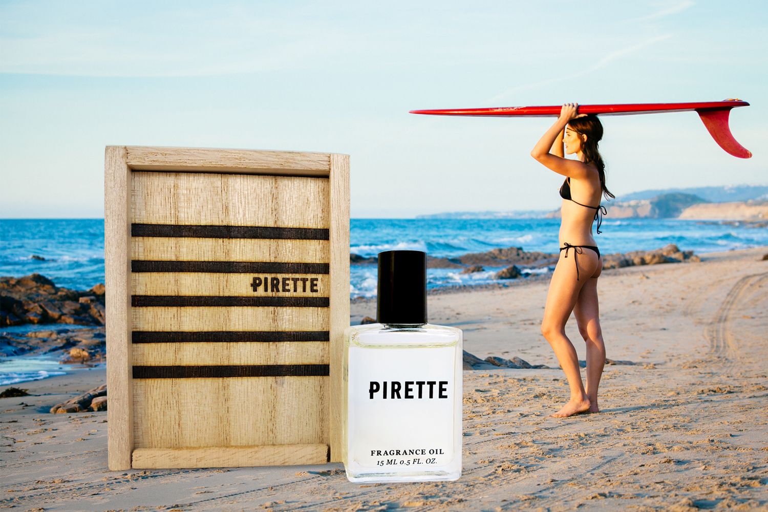 Pirette Fragrance Oil and box with young woman and red surf board over her head overlooking the beach and ocean at sunset