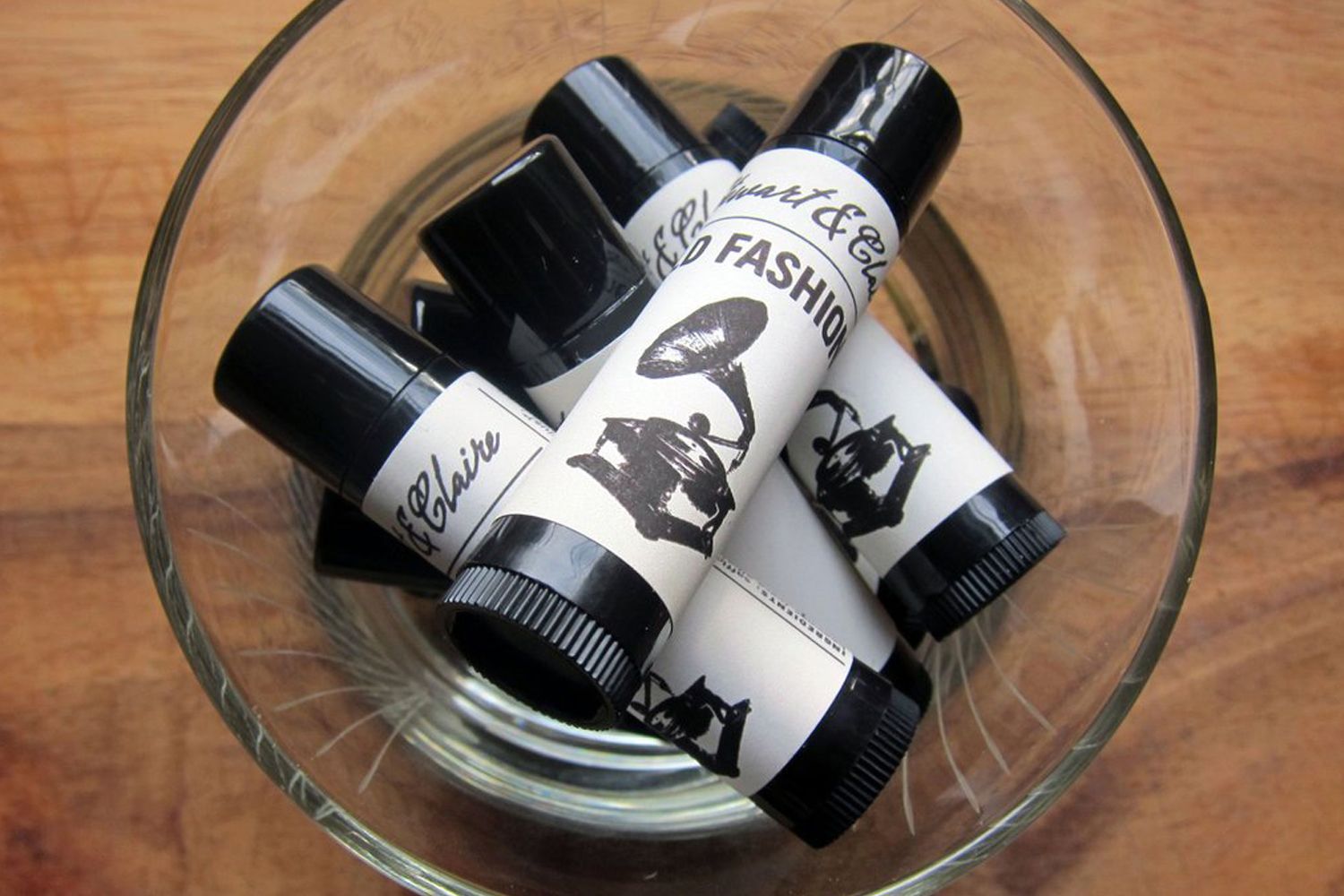 A selection of Stewart & Claire Lip balms tope view in clear glass bowl with wood background