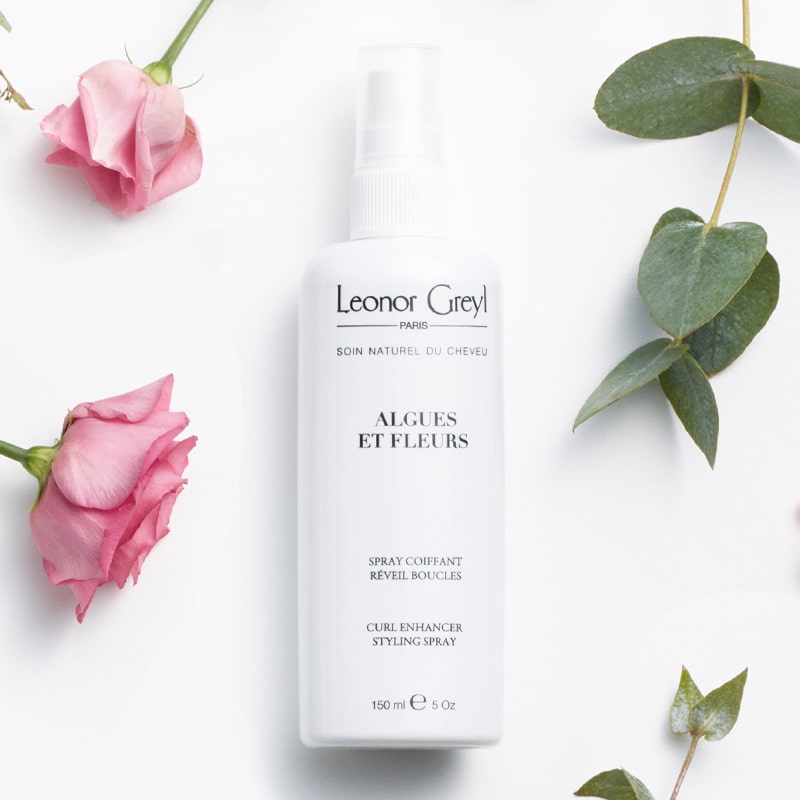 Lifestyle shot of Leonor Greyl Algues et Fleurs Conditioner Curl Enhancer Styling Spray (150 ml) with pink roses and leaves in the background