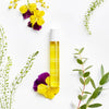 Lifestyle shot top view of Leonor Greyl Regenerescence Naturelle (20 ml) with yellow and purple flowers and green leaves in the background