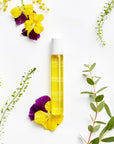 Lifestyle shot top view of Leonor Greyl Regenerescence Naturelle (20 ml) with yellow and purple flowers and green leaves in the background