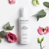 Lifestyle shot top view of Leonor Greyl Spray Structure Naturelle (150 ml) with pink flowers and leaves in the background