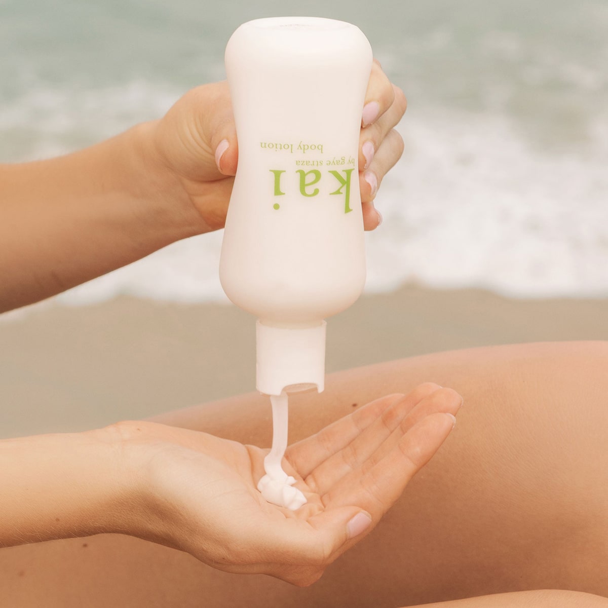Person applying Kai Fragrance Body Lotion (8 oz) on their hand with a beach background.