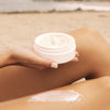 Person applying Kai Fragrance Body Butter (6.4 oz) to their leg on a beach.