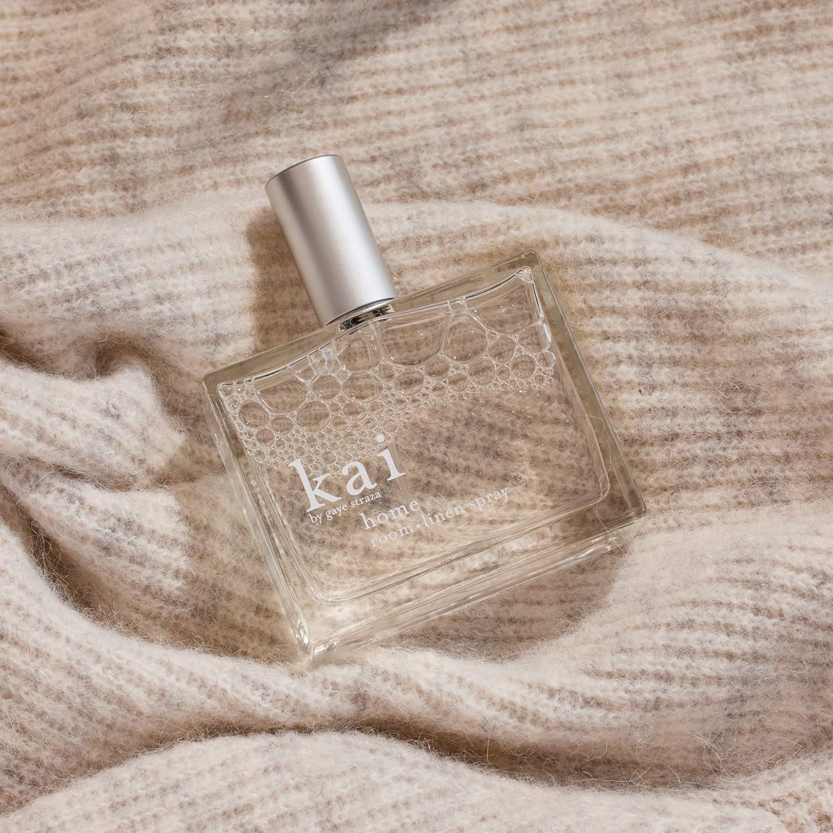 Kai Fragrance Home Room & Linen Spray (100 ml) with silver cap on a beige textured fabric background