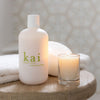 Lifestyle shot of Kai Fragrance Bathing Bubbles (12 oz) on a wooden surface next to burning candle (sold separately)