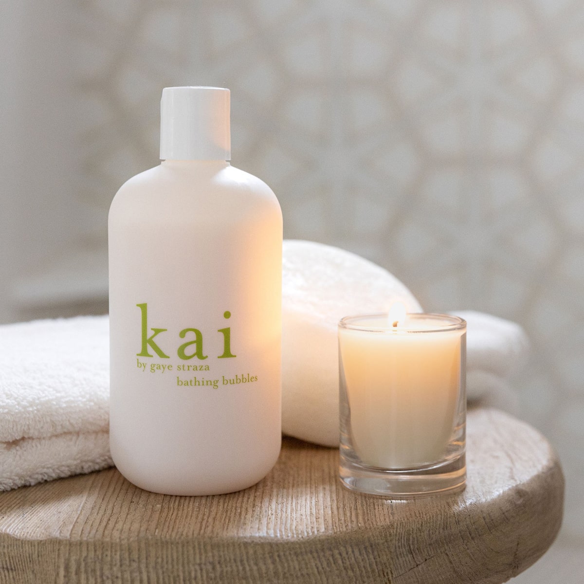 Lifestyle shot of Kai Fragrance Bathing Bubbles (12 oz) on a wooden surface next to burning candle (sold separately)