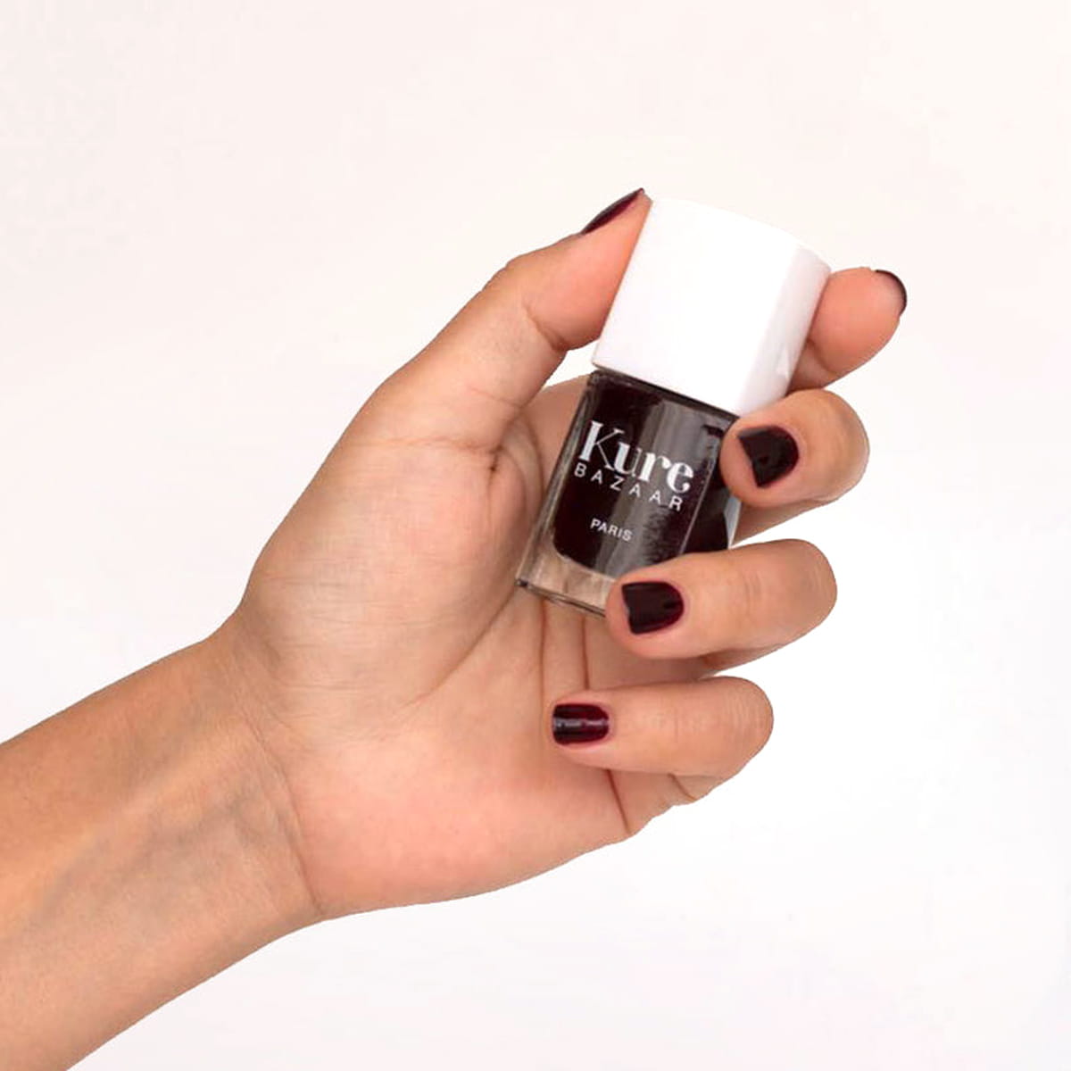 Close up of model wearing and holding bottle of Kure Bazaar Nail Lacquer - Scandal (10 ml)