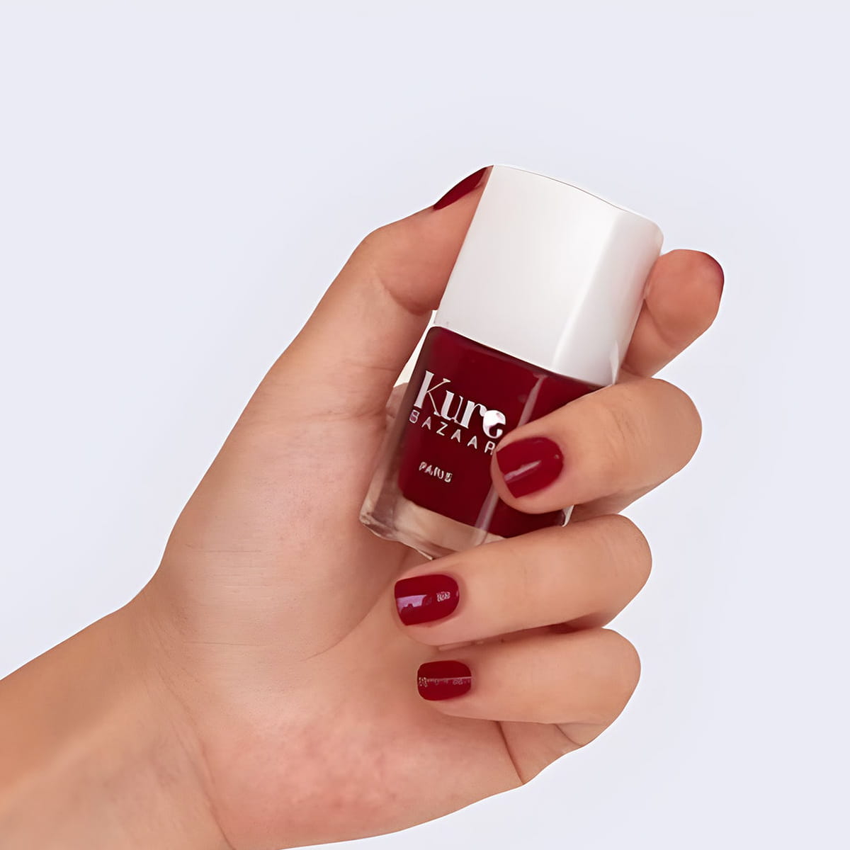 Close up of model wearing and holding bottle of Kure Bazaar Nail Lacquer - Cherie (10 ml)