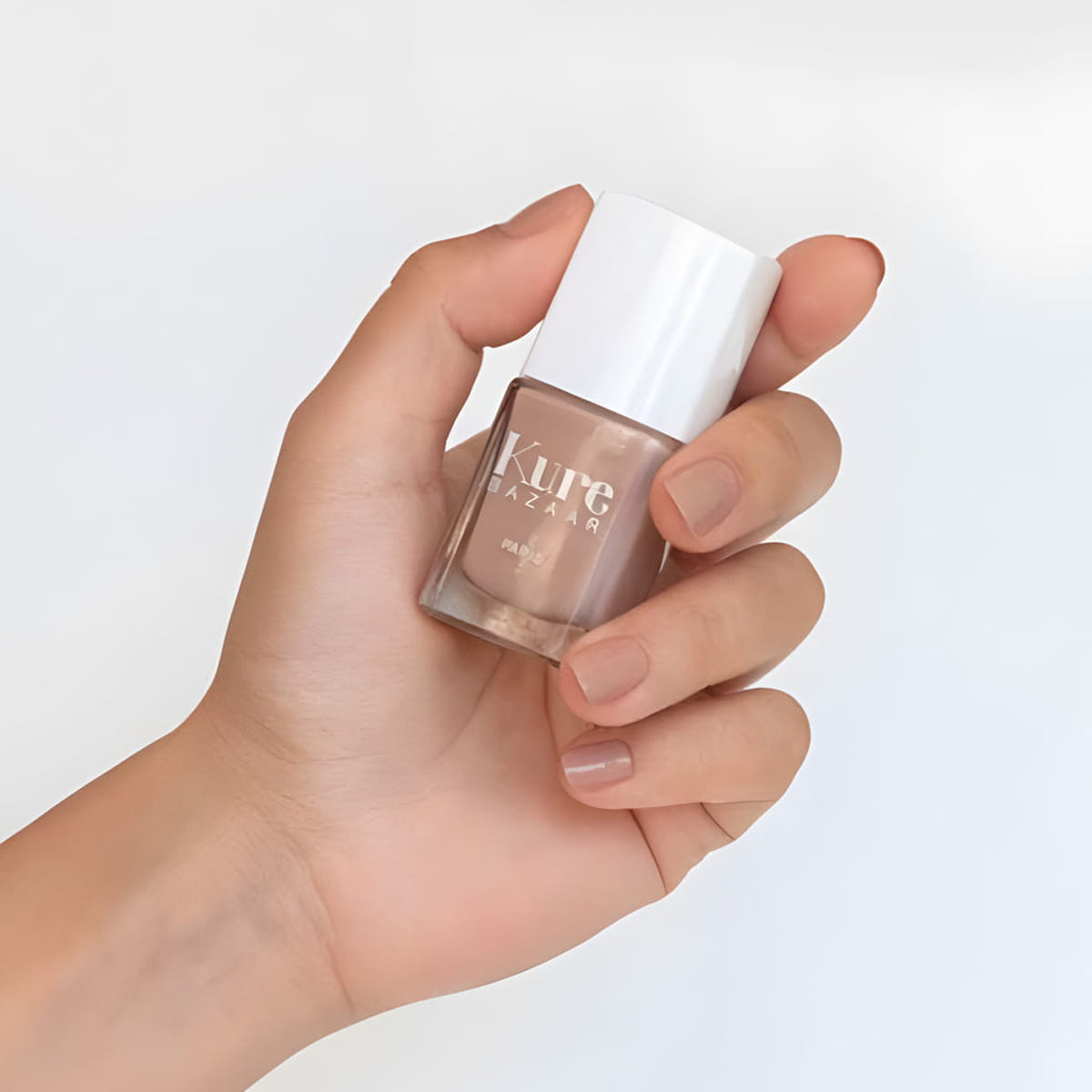 Close up of model wearing Kure Bazaar Nail Lacquer - Cappuccino (10 ml) and holding bottle