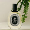 Diptyque L'Ombre Dans L'eau Eau de Toilette (100 ml) - product shown on creme background with green leaves. 